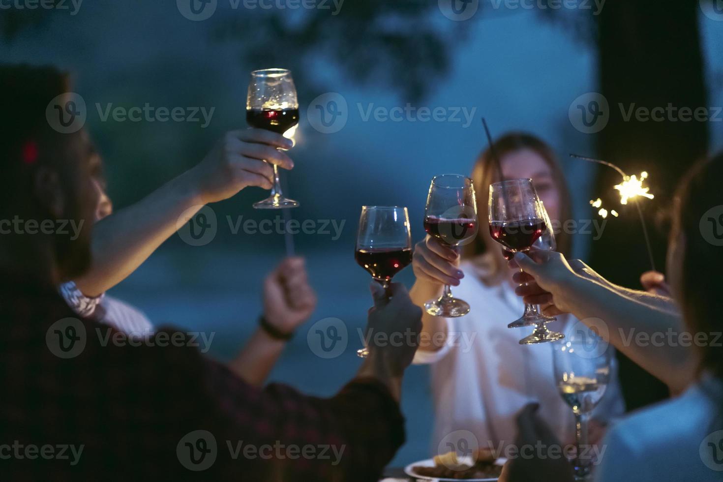 freunde, die rotweinglas toasten, während sie ein französisches picknick-abendessen im freien haben foto