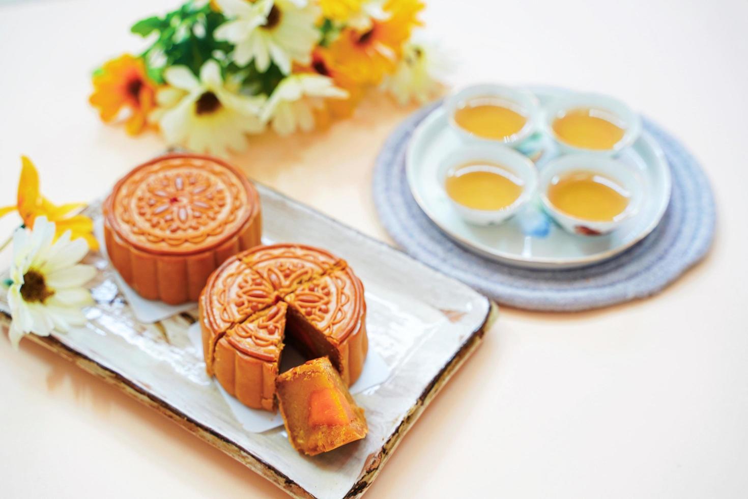 Draufsicht auf chinesischen Mondkuchen mit heißem Tee und Blumen auf gelbem Hintergrund, Feiertags- und Festivalkonzept foto