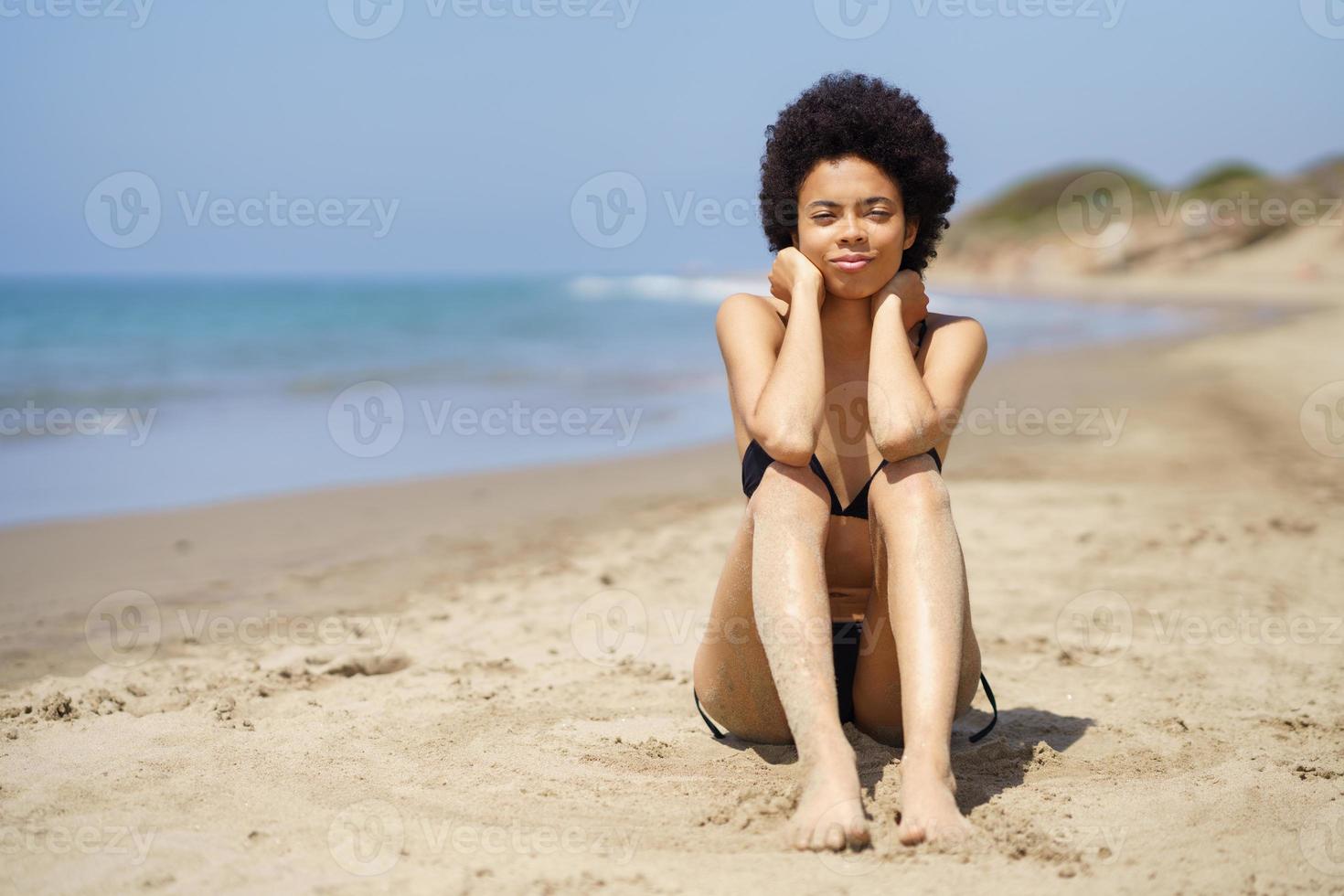 Schwarze Frau, die im Sommer am Sandstrand sitzt foto