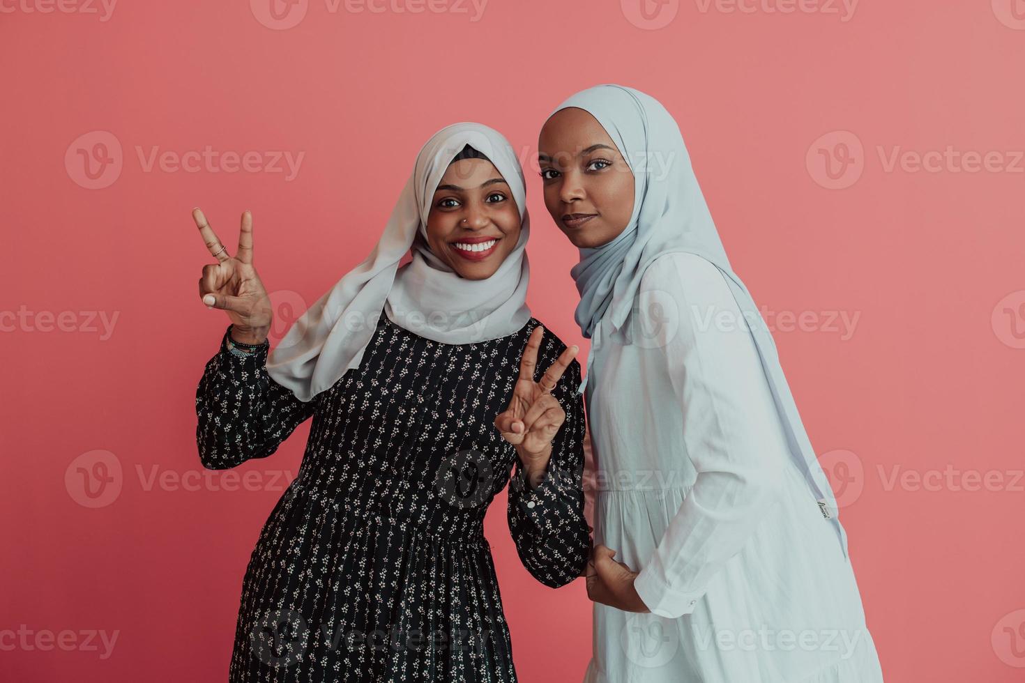 porträt von zwei jungen modernen muslimischen afro-schönheiten, die traditionelle islamische kleidung auf rosa hintergrund tragen foto