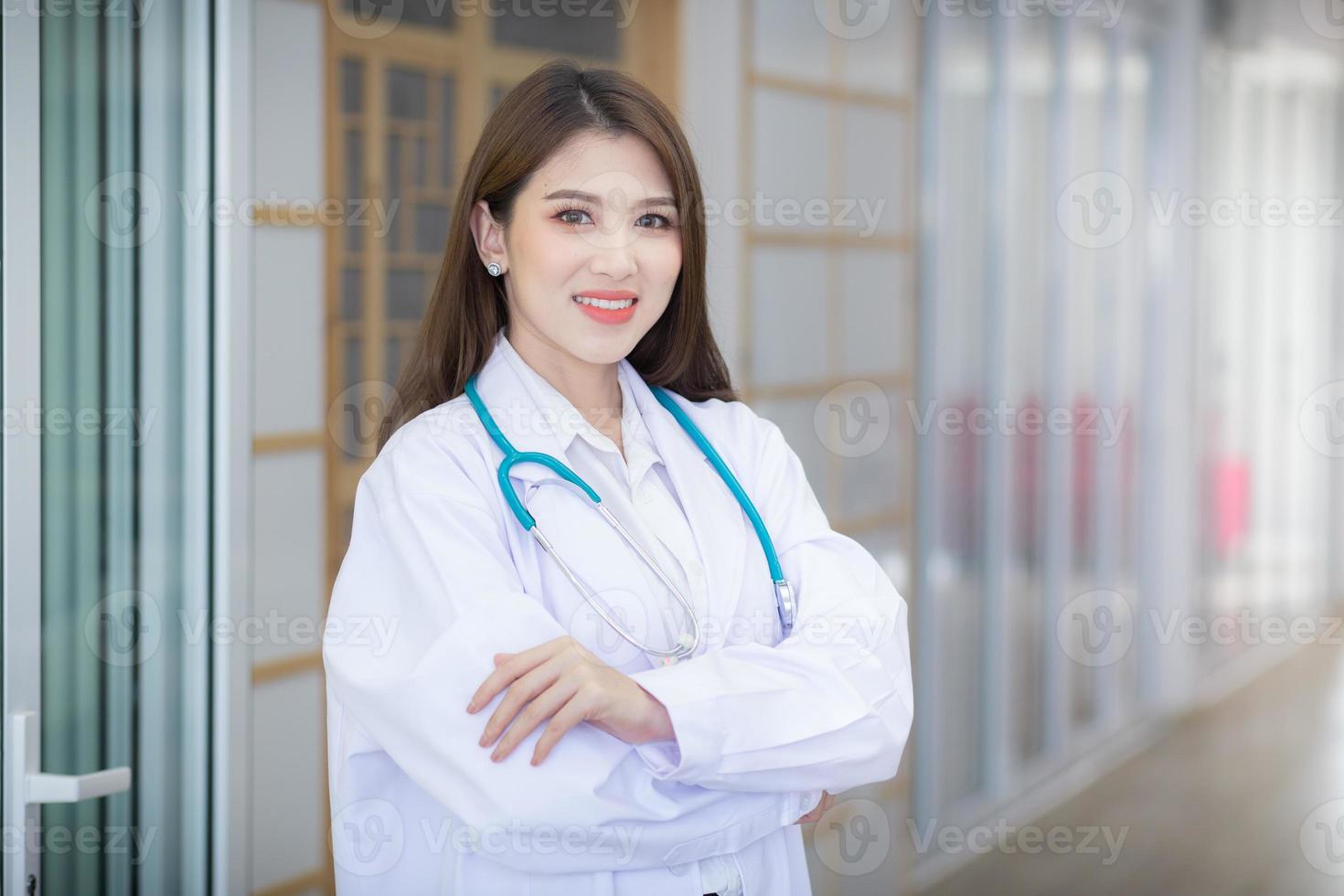 Junge schöne asiatische Ärztin steht mit verschränkten Armen glücklich und lächelt im Krankenhaus. trägt ein weißes Gewand und ein Stethoskop foto