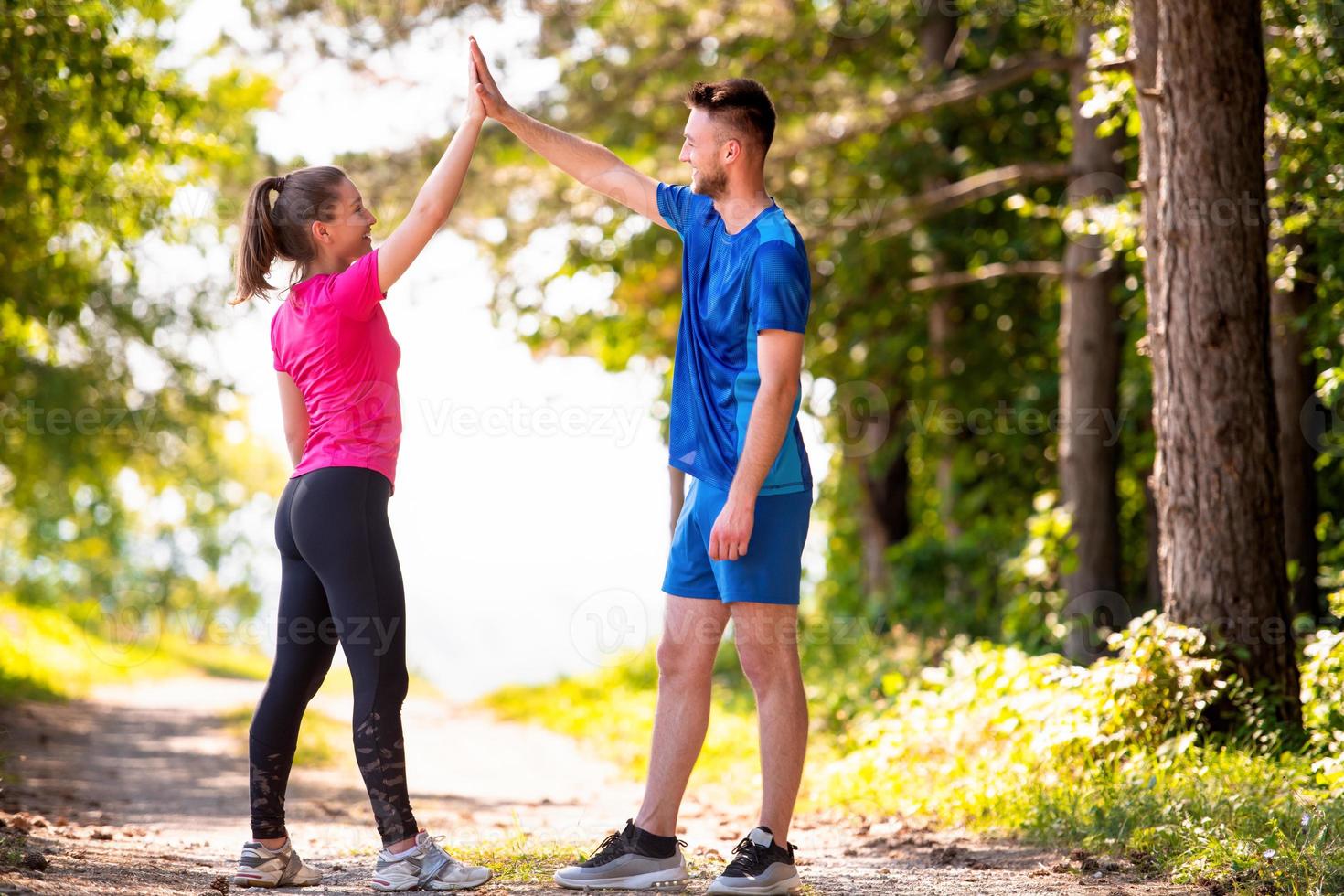 Joggendes Paar, das sich an einem sonnigen Tag in der Natur High Five gibt foto