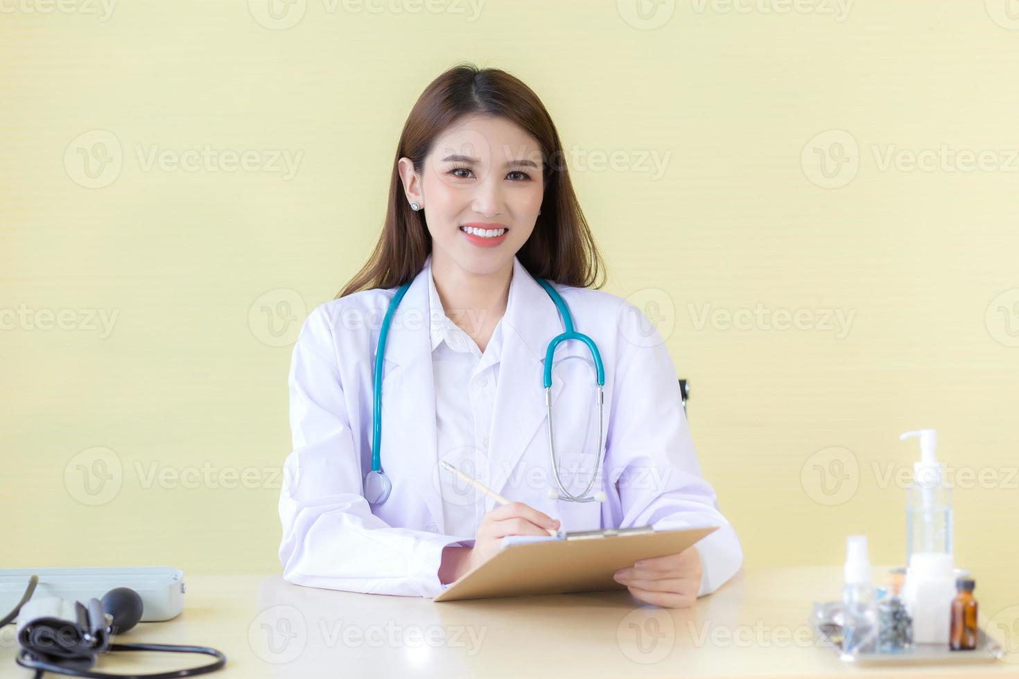 Schöne asiatische Ärztin, die im Krankenhaus sitzt und ein weißes Gewand und ein Stethoskop trägt foto