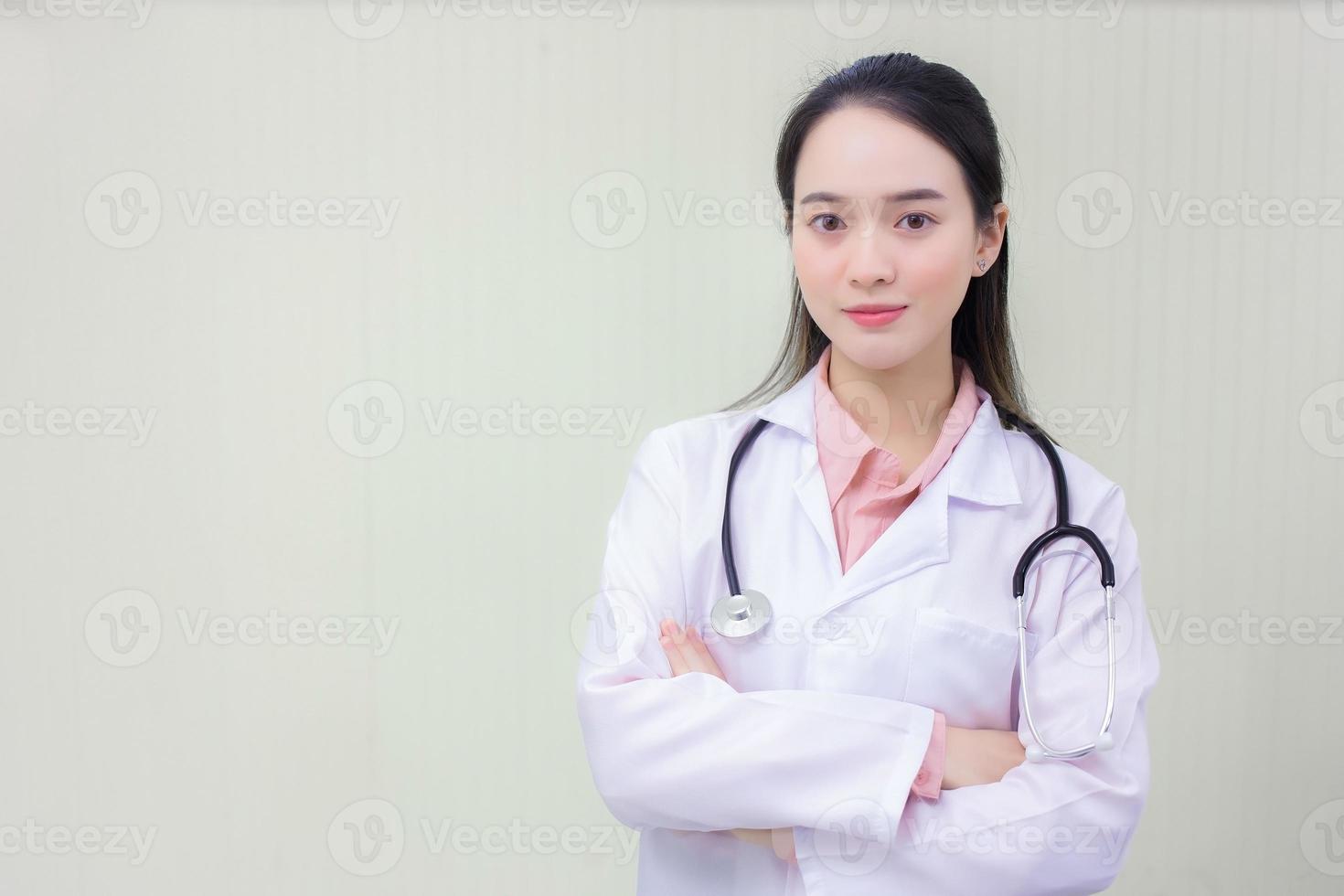 Junge schöne asiatische Ärztin steht mit verschränkten Armen glücklich und lächelt im Krankenhaus. trägt ein weißes Gewand und ein Stethoskop foto