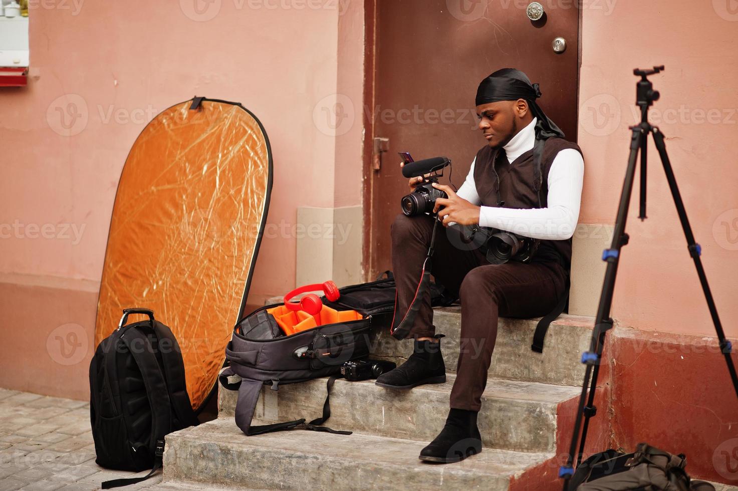 junger professioneller afroamerikanischer videofilmer mit professioneller kamera mit professioneller ausrüstung. Afro-Kameramann mit schwarzem Duraq, der Videos macht. foto