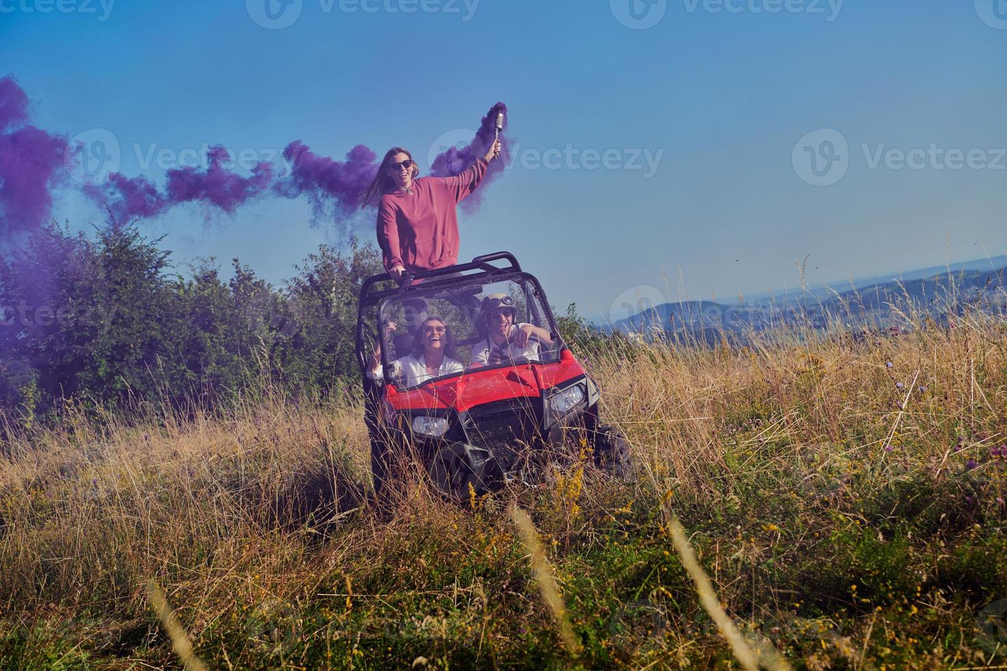 Aufgeregte Menschen, die Spaß daran haben, einen schönen sonnigen Tag mit bunten Fackeln zu genießen, während sie ein Offroad-Buggy-Auto fahren foto