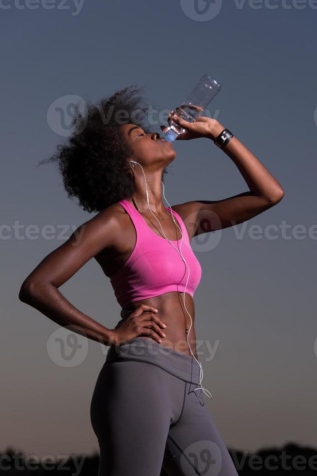 Afroamerikanerin trinkt Wasser nach dem Joggen in der Natur foto