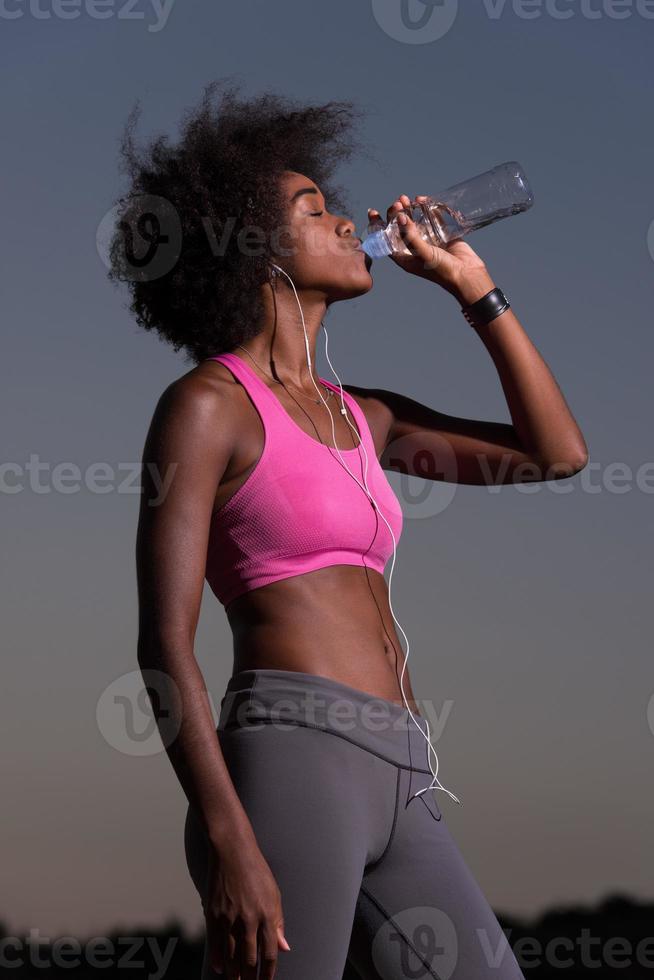 Afroamerikanerin trinkt Wasser nach dem Joggen in der Natur foto