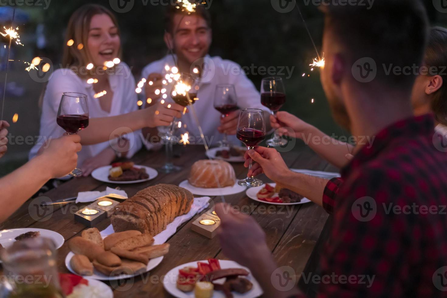 freunde, die rotweinglas toasten, während sie ein französisches picknick-abendessen im freien haben foto
