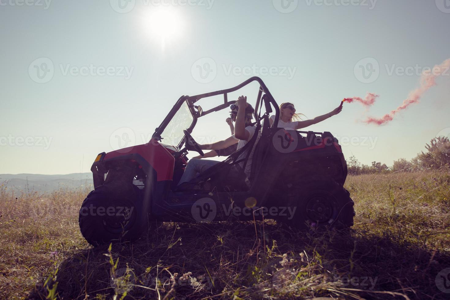 Aufgeregte Menschen, die Spaß daran haben, einen schönen sonnigen Tag mit bunten Fackeln zu genießen, während sie ein Offroad-Buggy-Auto fahren foto