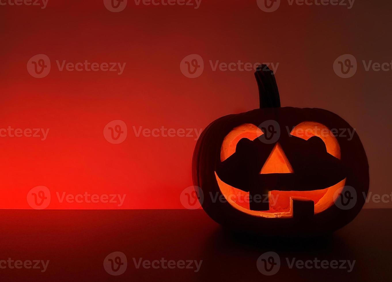 Geschnitzter leuchtender Kürbis steht in dunkler Nacht auf der Oberfläche. die Rückwand mit Platz für Text ist rot hervorgehoben. halloween-feiertagshintergrund mit traditioneller lächelnder jack-o-laterne. foto