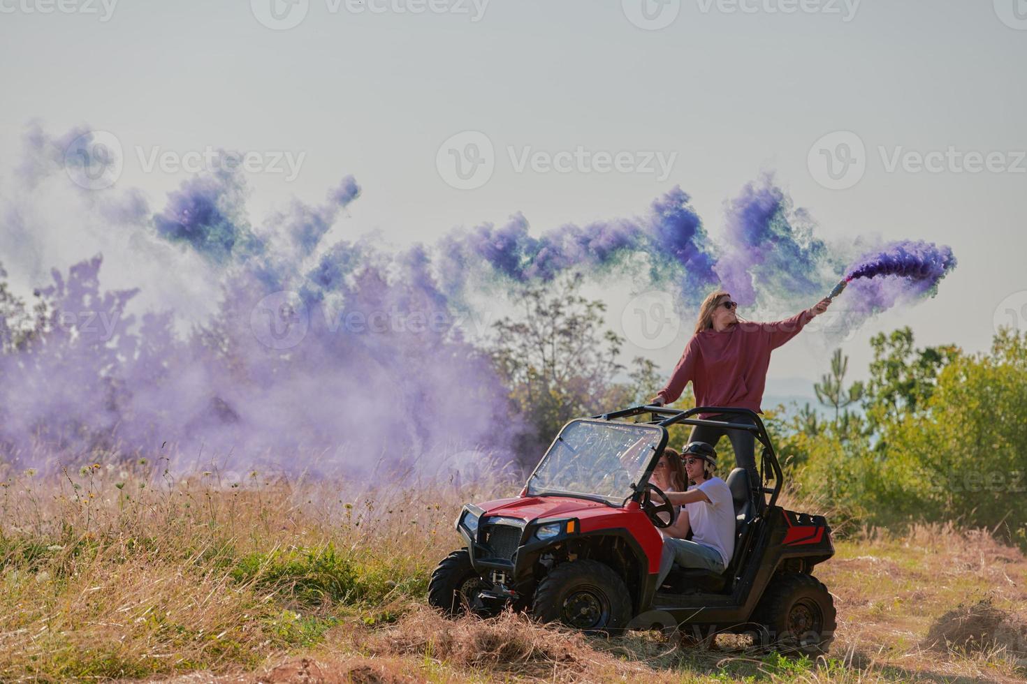 Aufgeregte Menschen, die Spaß daran haben, einen schönen sonnigen Tag mit bunten Fackeln zu genießen, während sie ein Offroad-Buggy-Auto fahren foto