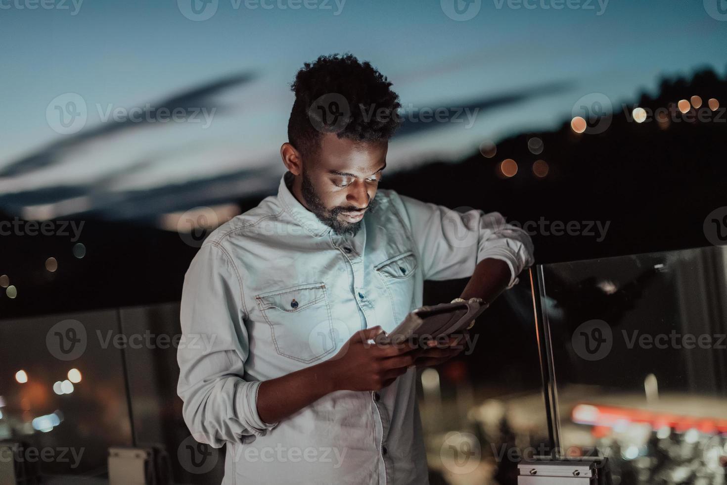 der junge mann auf einer städtischen straße in der nacht schreibt auf dem smartphone mit bokeh und neonlichtern der stadt im hintergrund. foto