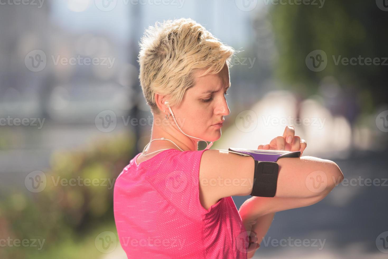 Joggende Frau, die vor dem Joggen das Telefon einstellt foto