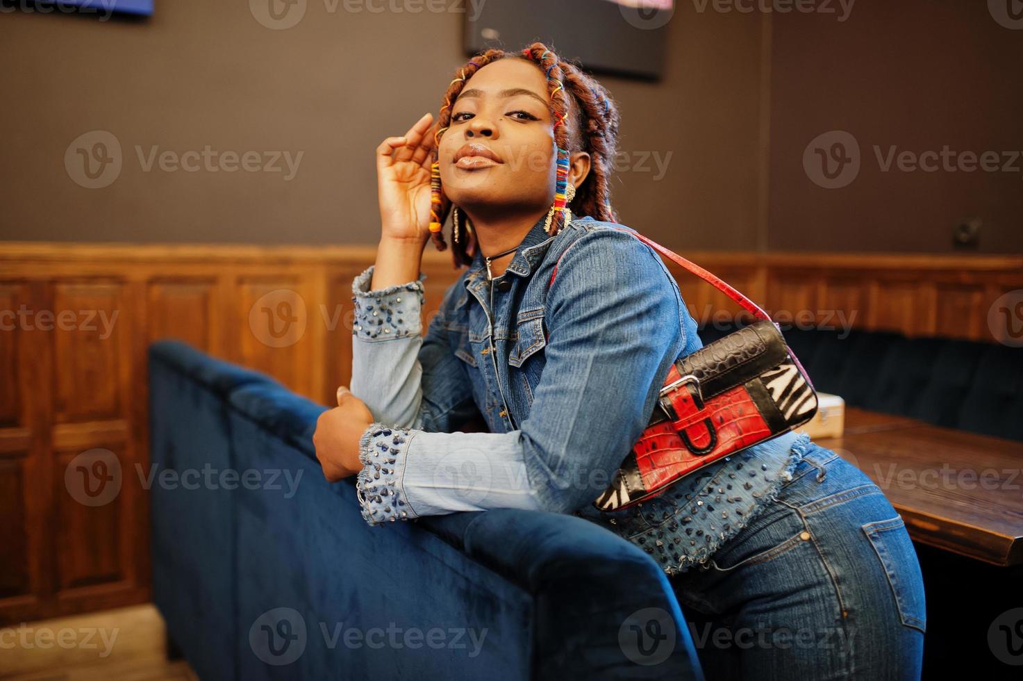 Schöne afroamerikanische Frau mit Dreadlocks in blauer, stylischer Jeansjacke im Café. schönes cooles modisches schwarzes junges mädchen drinnen. foto