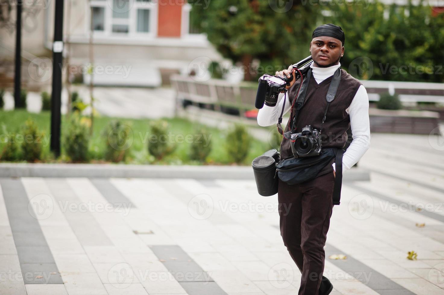 junger professioneller afroamerikanischer videofilmer mit professioneller kamera mit professioneller ausrüstung. Afro-Kameramann mit schwarzem Duraq, der Videos macht. foto