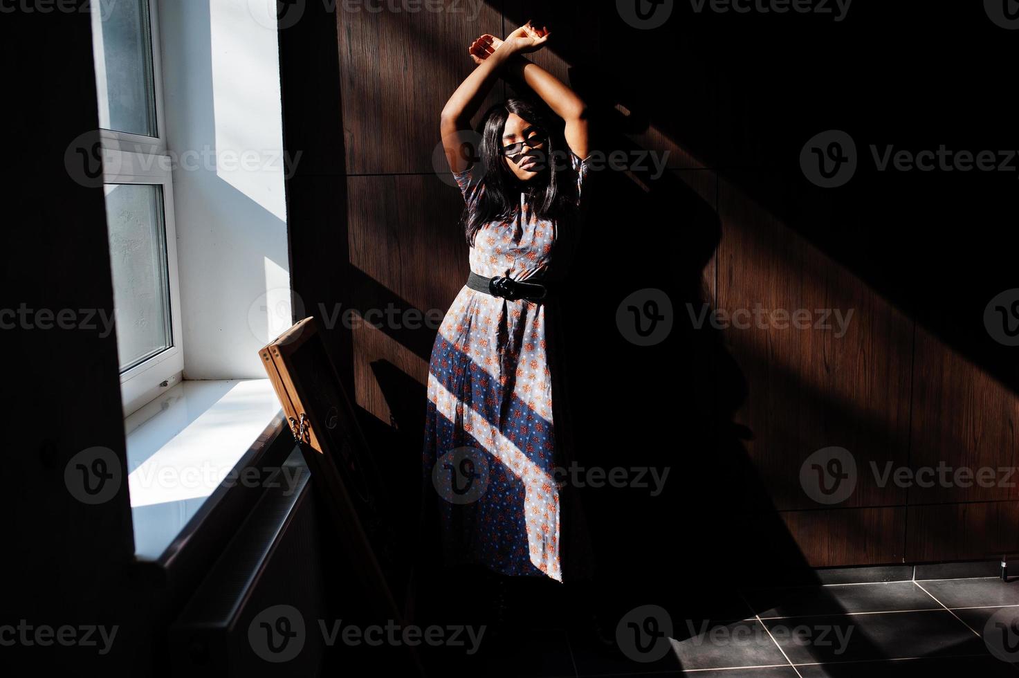 Spiel mit Schatten. Modeporträt einer afroamerikanischen Frau in langem Kleid und Brille im Innenbereich. foto