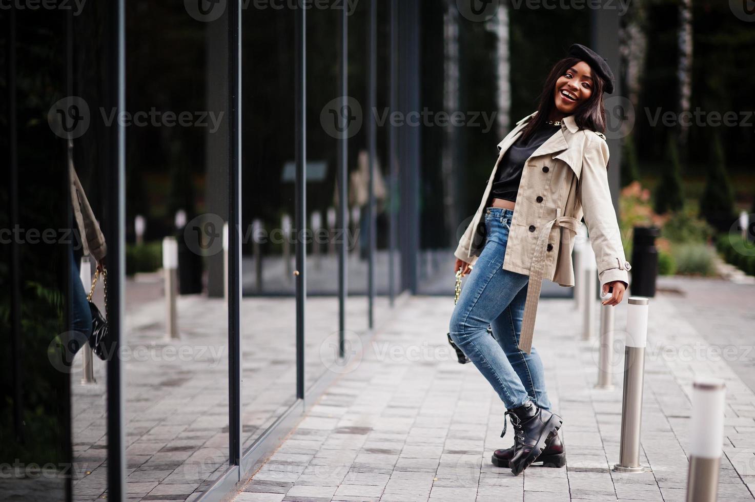 modische afroamerikanische frau trägt baskenmütze und mantel mit handtasche, die im freien posiert. foto