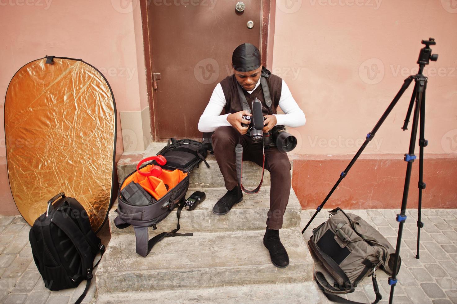 junger professioneller afroamerikanischer videofilmer mit professioneller kamera mit professioneller ausrüstung. Afro-Kameramann mit schwarzem Duraq, der Videos macht. foto