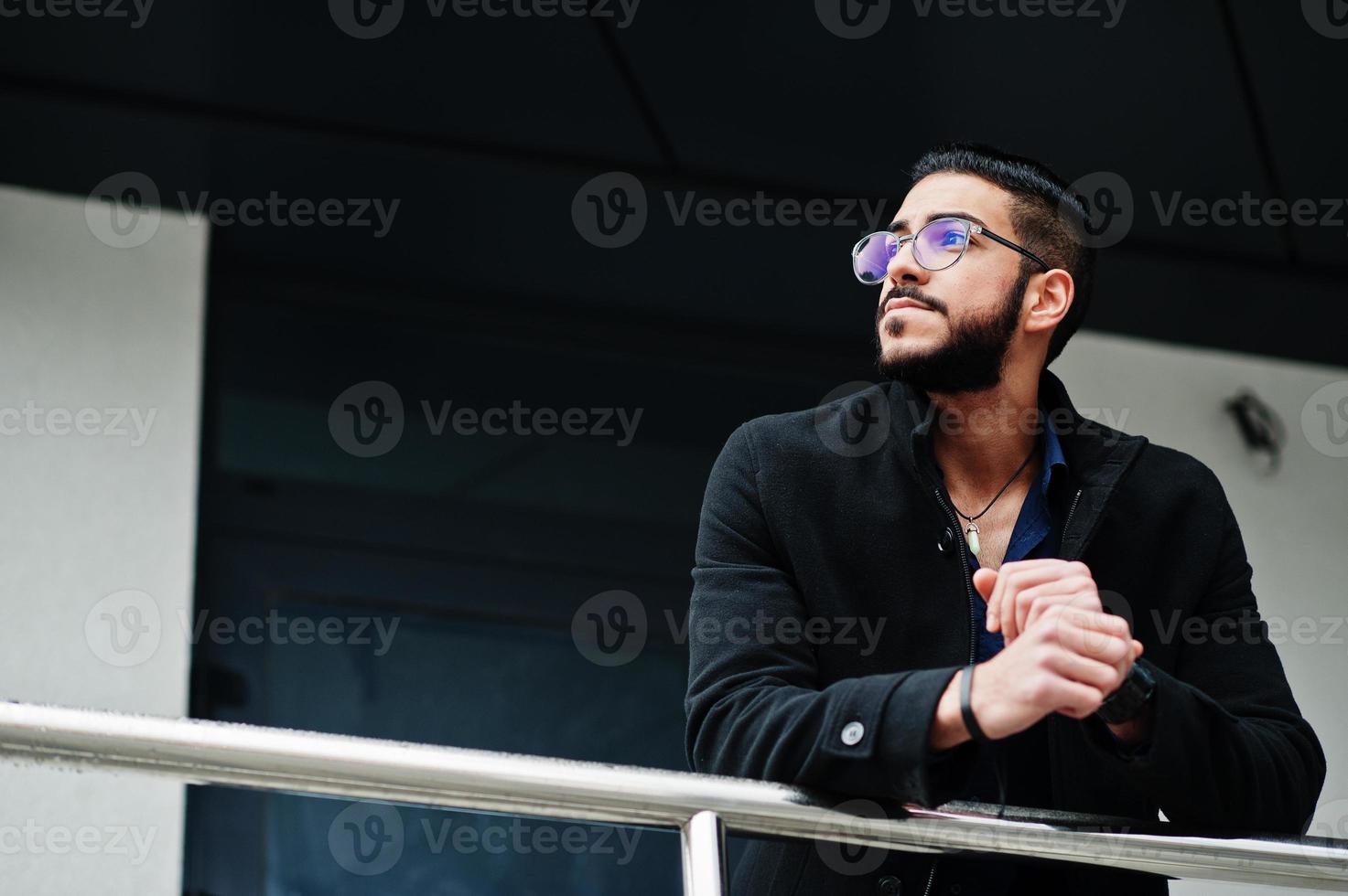 Unternehmer aus dem Nahen Osten tragen einen schwarzen Mantel und ein blaues Hemd, eine Brille gegen ein Bürogebäude. foto