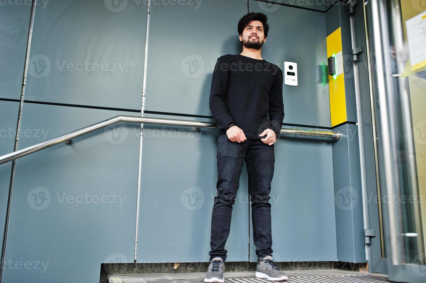 Urbaner junger Hipster-Indianer, der ganz in Schwarz gekleidet ist, steht in der Nähe des Code-Eingangs. cooler Südasiate. foto