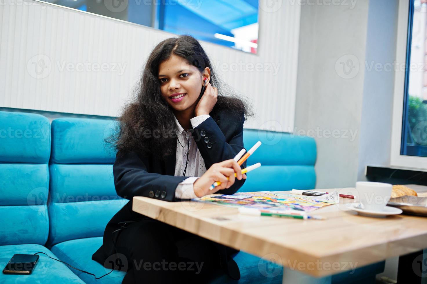 Indische Künstlerin trägt formelles Farbbild und hört hinduistische Musik aus Kopfhörern, während sie im Café sitzt. foto
