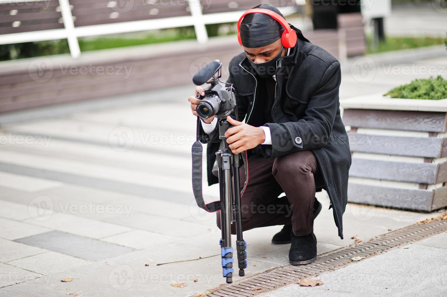 junger professioneller afroamerikanischer videofilmer mit professioneller kamera mit professioneller ausrüstung. afro-kameramann mit schwarzem duraq und gesichtsschutzmaske, der ein video macht. foto