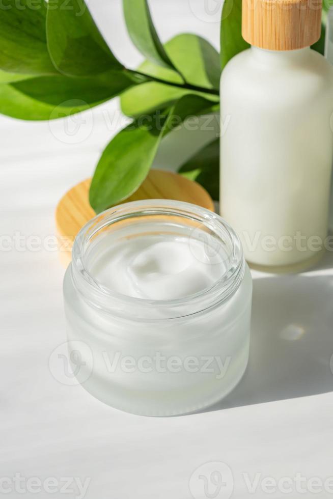Naturkosmetik-Set. Feuchtigkeitscreme in umweltfreundlichem Glas mit Bambusdeckel, Serum in Tropfflasche im Vordergrund. Verpackungsdesign für Bio-Hautpflegeprodukte mit grünen Blättern. foto