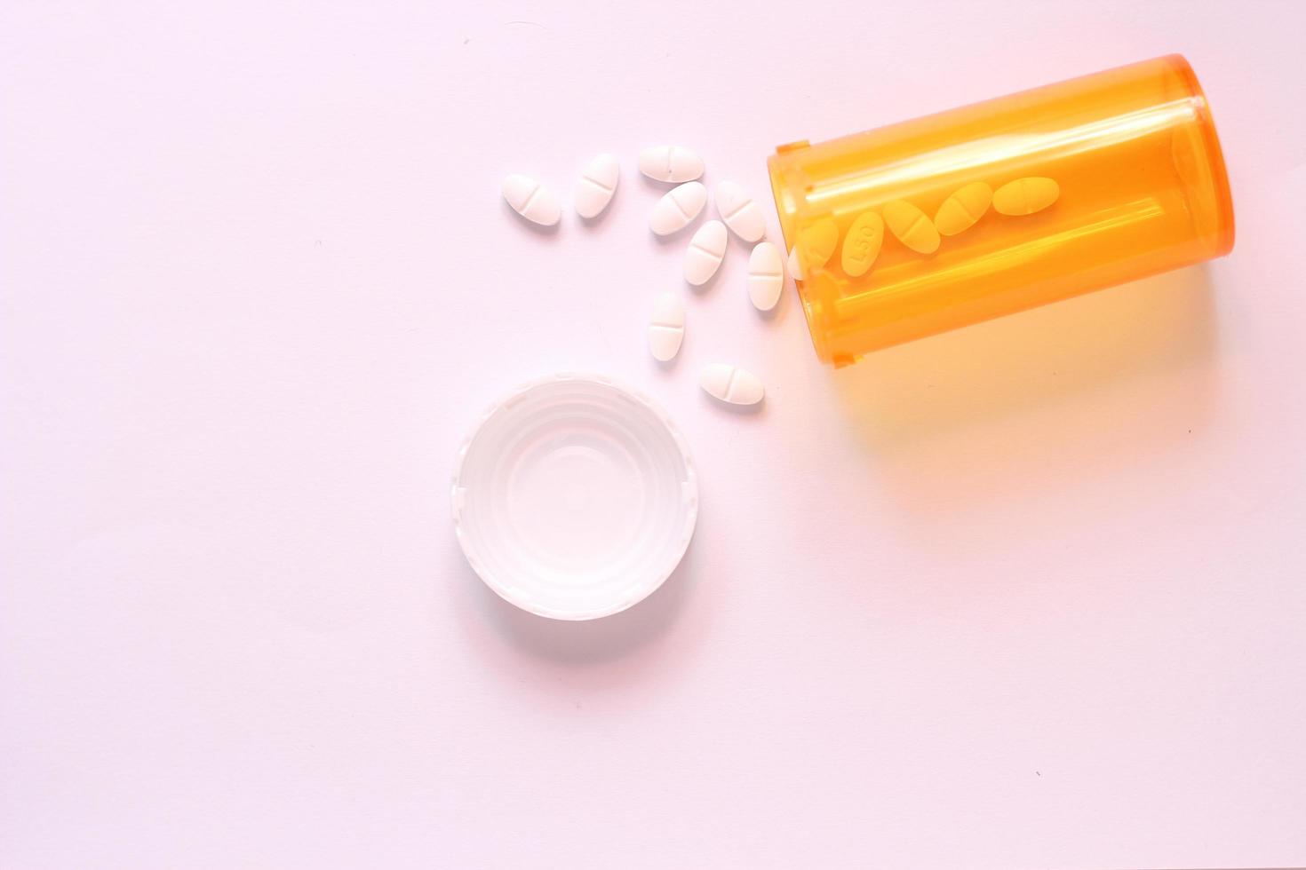 ovale Pillen und orangefarbene Tablettenfläschchen waren auf der weißen Tischplatte ausgebreitet. foto