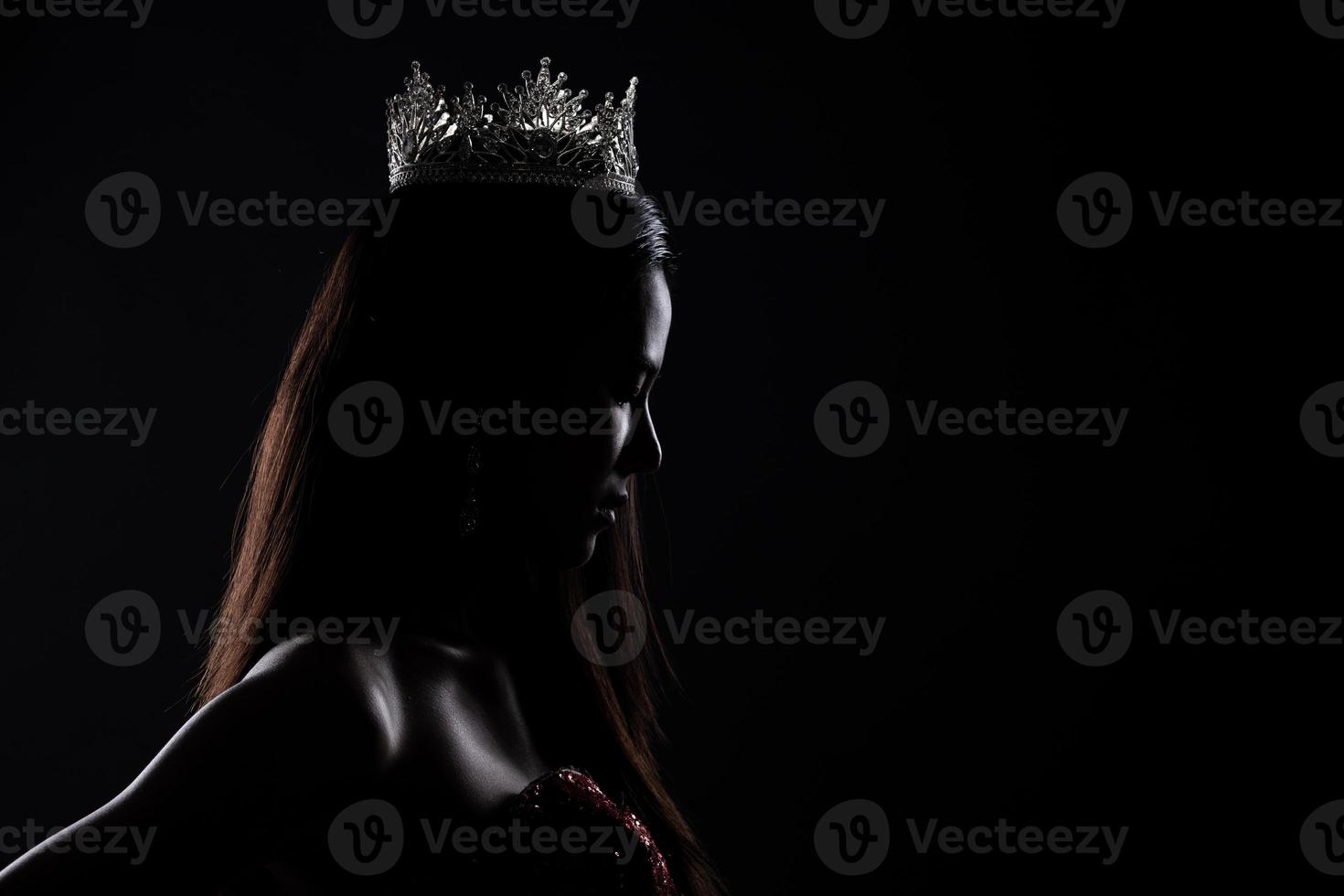 Porträt des Miss-Schönheitswettbewerbs im Pailletten-Abend-Ballkleid, langes Kleid mit funkelnder, heller Diamantkrone, Silhouette, zurückhaltende Belichtung mit Vorhang, Studiobeleuchtung, dunkler Hintergrund, dramatisch foto