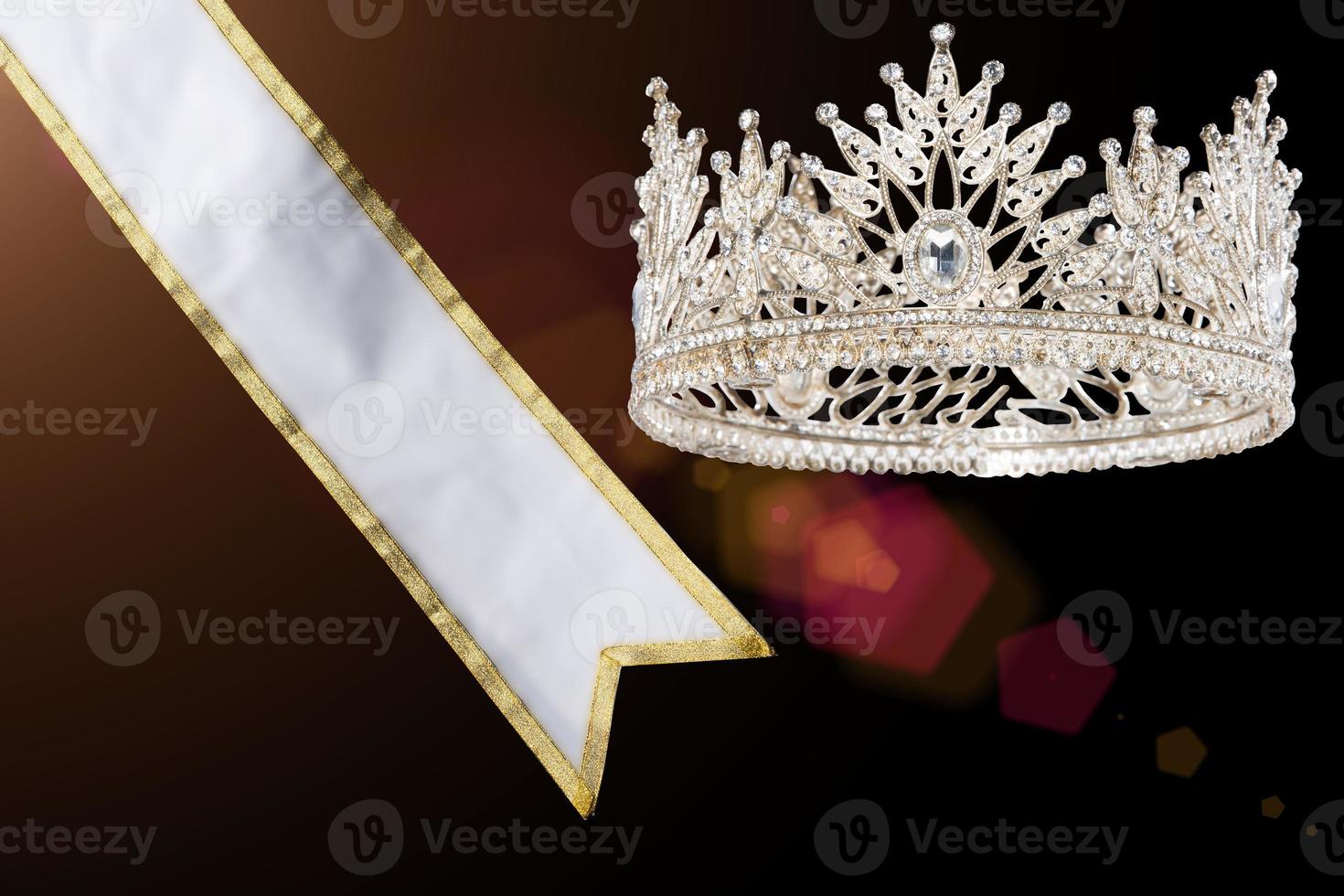 preisgekrönter Preis für den Gewinner des Schönheitswettbewerbs Miss Beauty Queen ist Schärpe, Diamantkrone, Studiobeleuchtung abstrakter dunkler drapierender Textilhintergrund foto