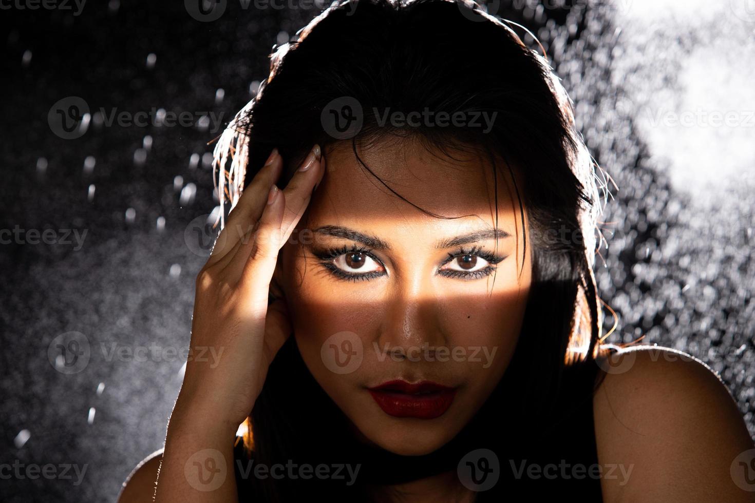 indische gebräunte haut asiatische frau zeigt gesichts-make-up mit hintergrundbeleuchtetem licht und wasserspritzerspray foto