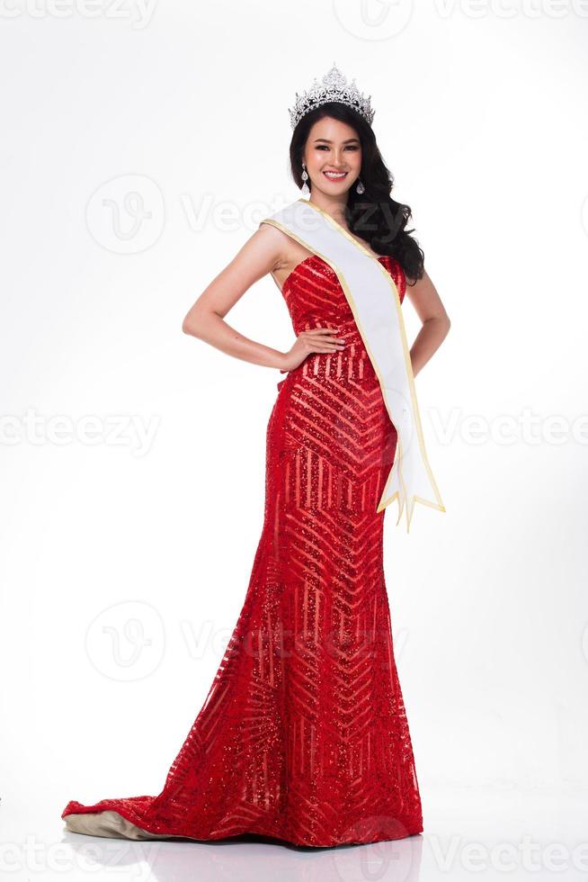 volle Länge des Miss-Wettbewerbs im asiatischen roten Pailletten-Abend-Ballkleidkleid mit silberner Diamant-Kronenschärpe, Mode-Make-up-Gesichtsfrisur, Studiobeleuchtung, weißer Hintergrund, isolierter Kopierraum foto