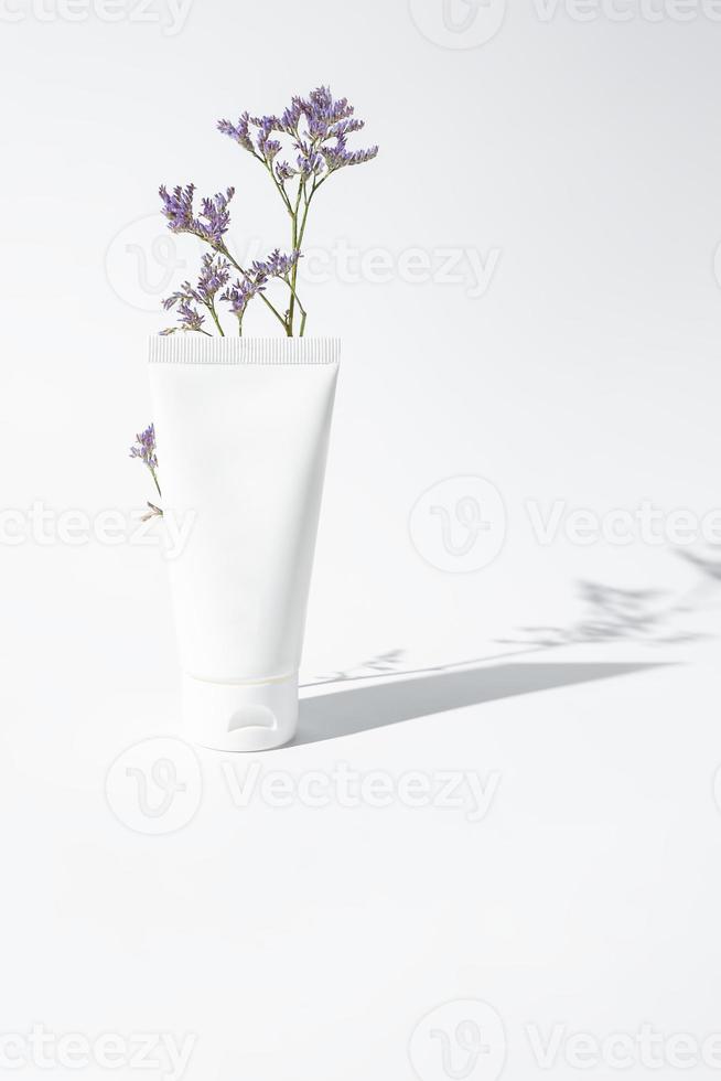 feuchtigkeitscreme handcreme weißes plastikrohrmodell auf weißem trandy hintergrund mit blume und harten schatten. leere Hautpflege-Schönheitsproduktverpackung foto