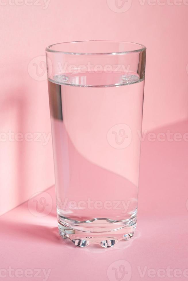 Nahaufnahme von Sprudelwasser in transparentem Hochglas und Sonnenblendung auf rosa Hintergrund foto