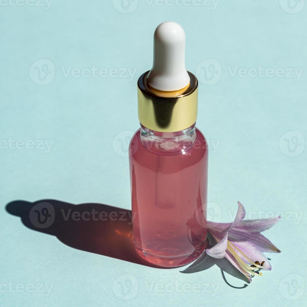 Kosmetikflasche aus Glas mit einer Pipette auf blauem Hintergrund. naturkosmetikkonzept, natürliches ätherisches rosenöl und hautpflegeprodukte foto