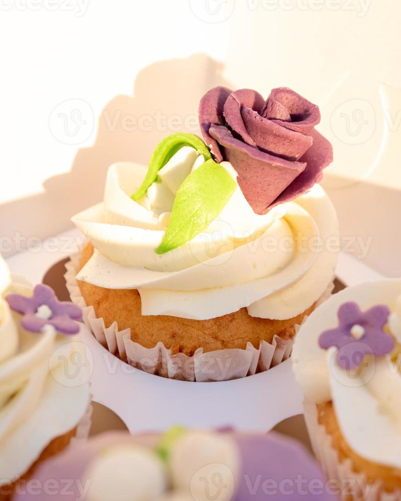 Papierschachtel mit Cupcakes. Weihnachtscupcakes mit Zuckerrose und Buttercreme. cupcakes verpackung, lieferkarton im hintergrund. Geschenkbox mit Süßigkeiten foto