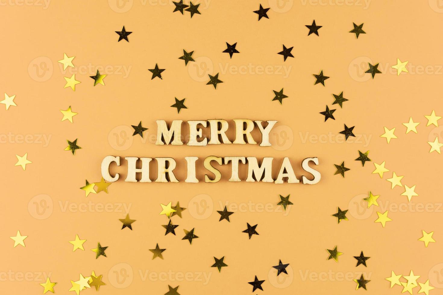 Holzbuchstaben auf beigem Hintergrund. frohe weihnachten schriftzug auf pastellpapier mit verstreuten sternkonfetti. festliche grußkarte. foto
