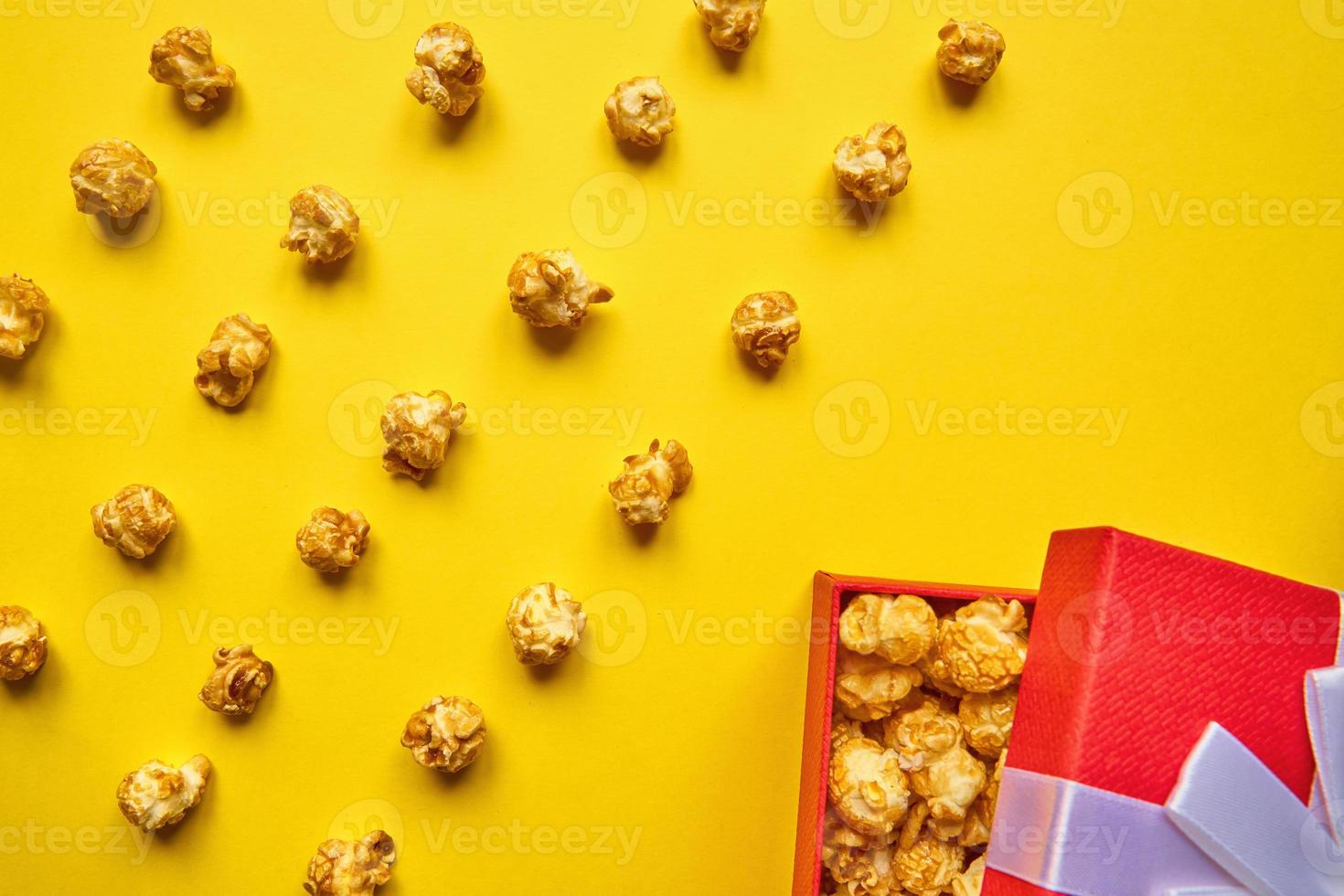 bunte trendige Kulisse mit Karamell-Popcorn und roter Geschenkbox auf gelbem Hintergrund foto