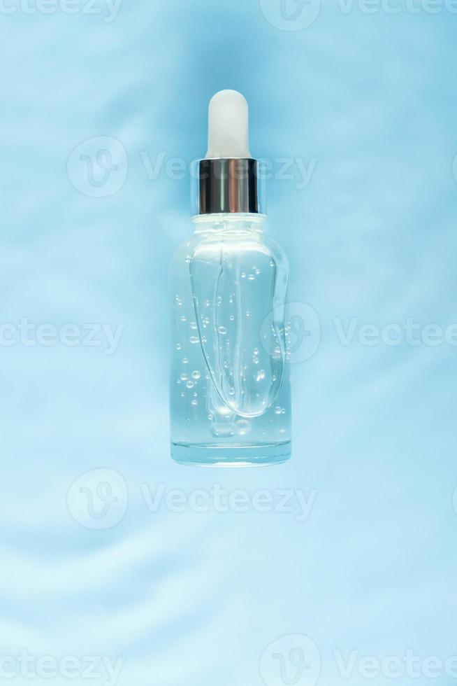 Serumglasflasche auf Wasser mit Tropfen Konzept der feuchtigkeitsspendenden Kosmetik mit natürlichem Meereskollagen. Hautpflege, Anti-Aging foto