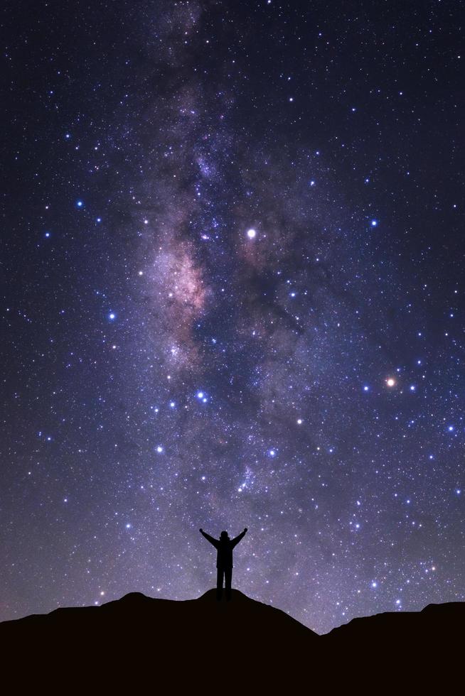 Milchstraßengalaxie mit Sternen und Weltraumstaub im Universum und Silhouette eines stehenden glücklichen Mannes foto