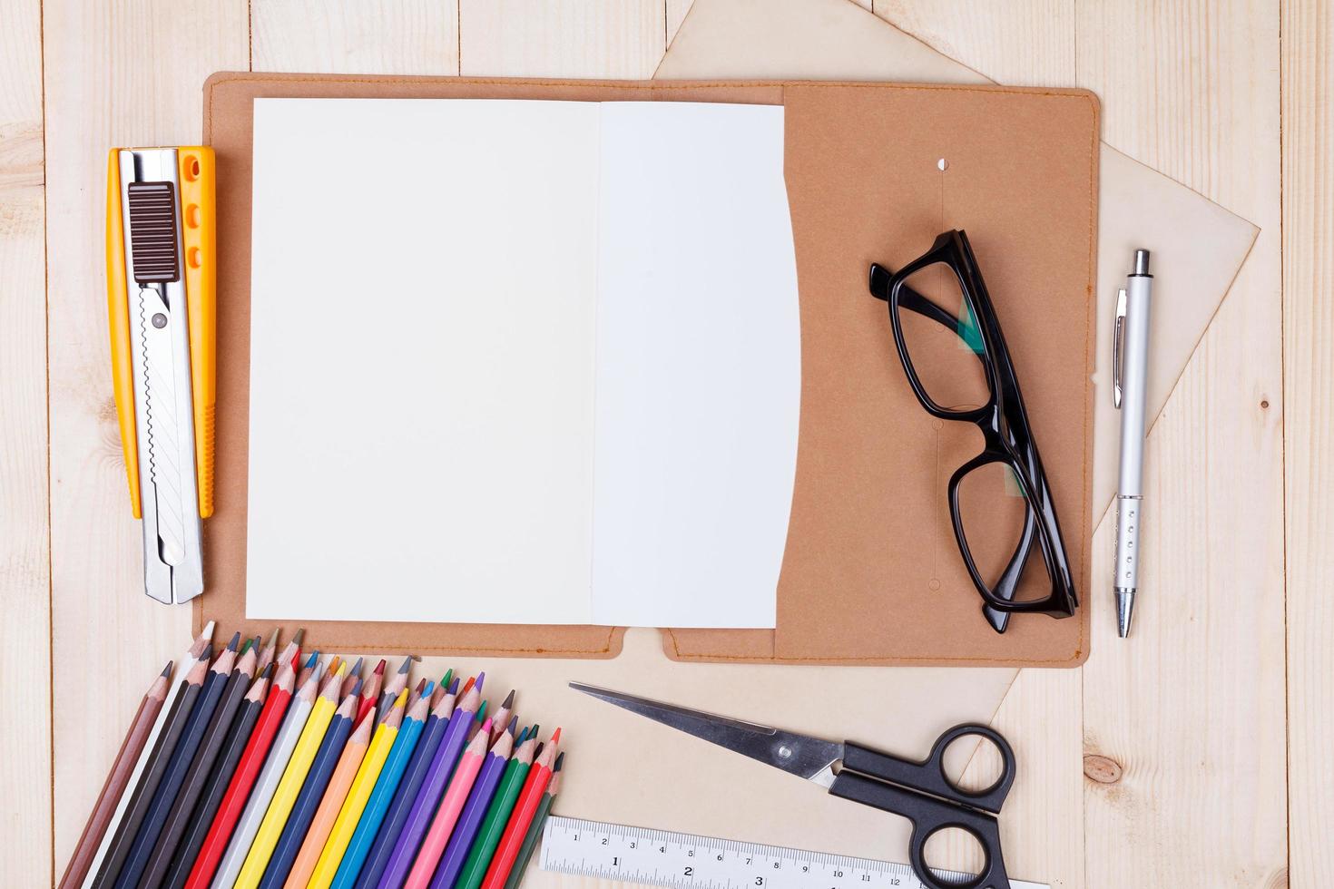 Arbeitsplatz mit Buntstiften und Zubehör, Notizbuch, Brille auf Holztisch foto