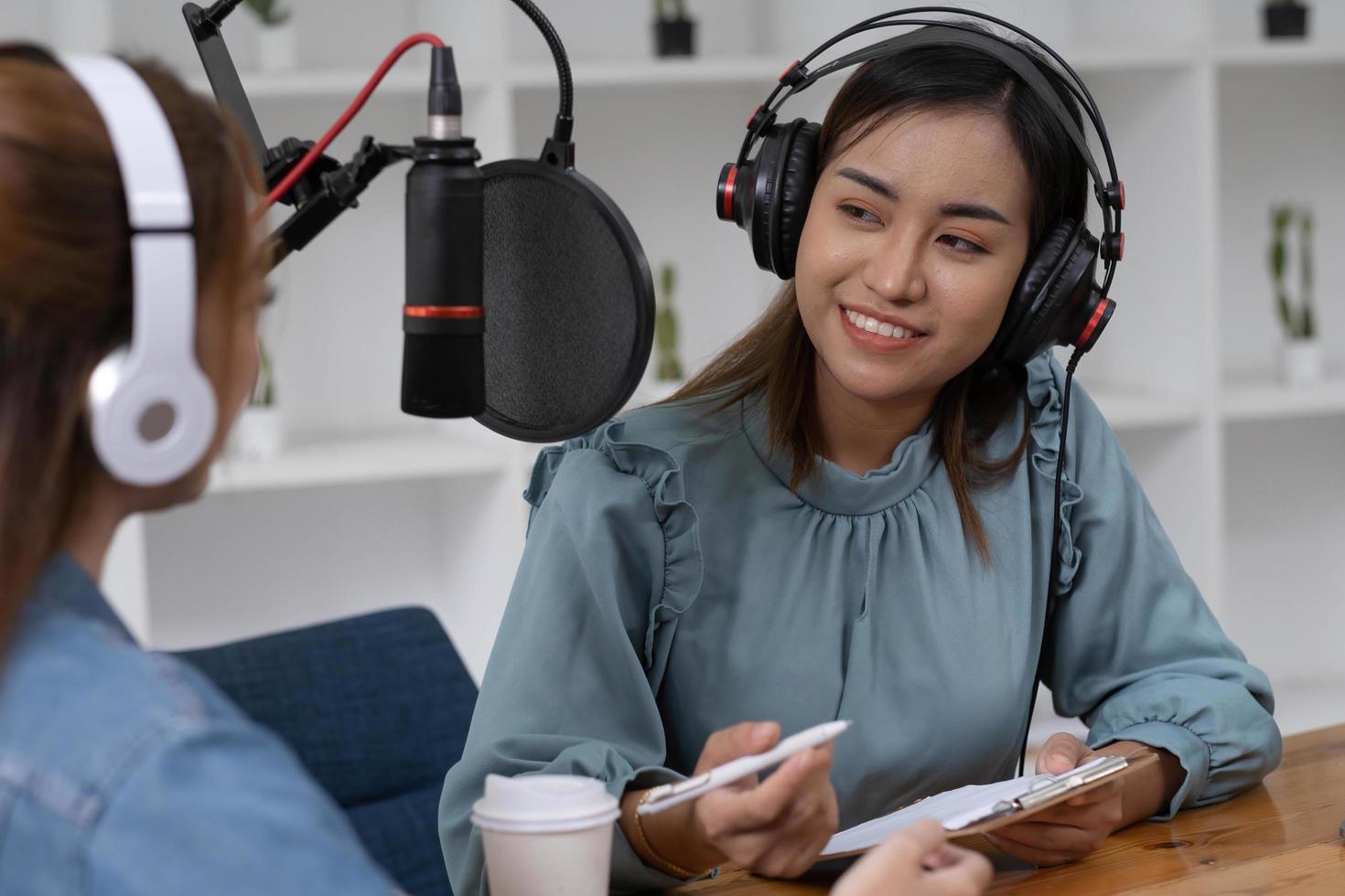 lächeln zwei asiatische junge frau, mann radiomoderatoren in kopfhörern, mikrofon beim sprechen, konversation, aufnahme von podcast im rundfunk im studio zusammen. technologie zur herstellung von audioaufzeichnungskonzepten. foto