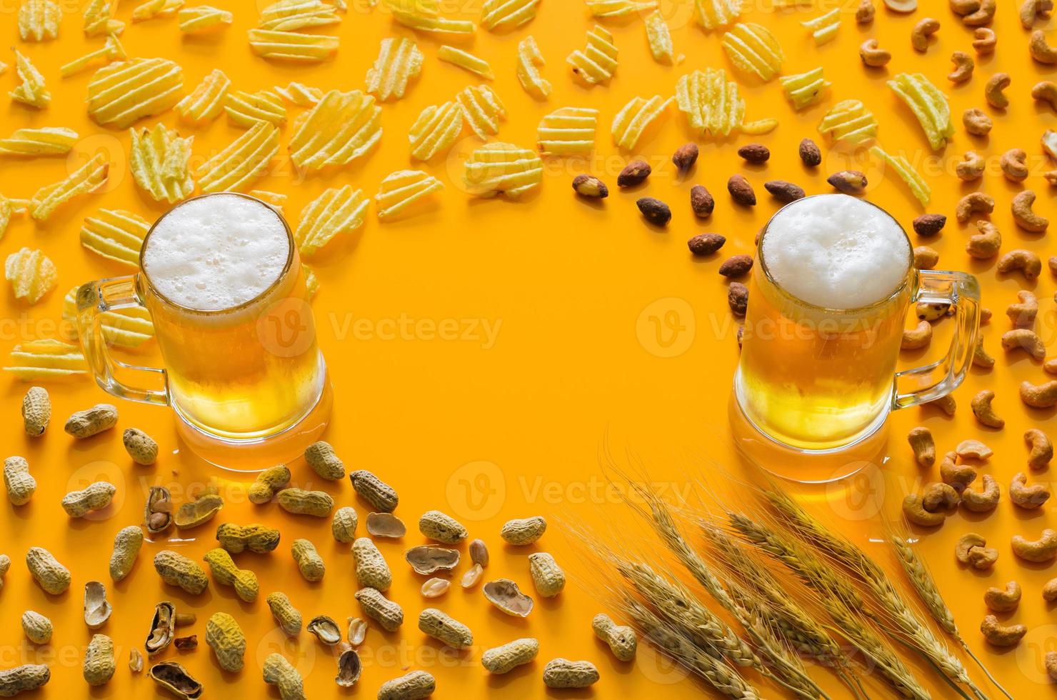 Zwei Gläser Bier mit Chips und Nüssen auf gelbem Hintergrund für das Oktoberfest-Konzept. foto