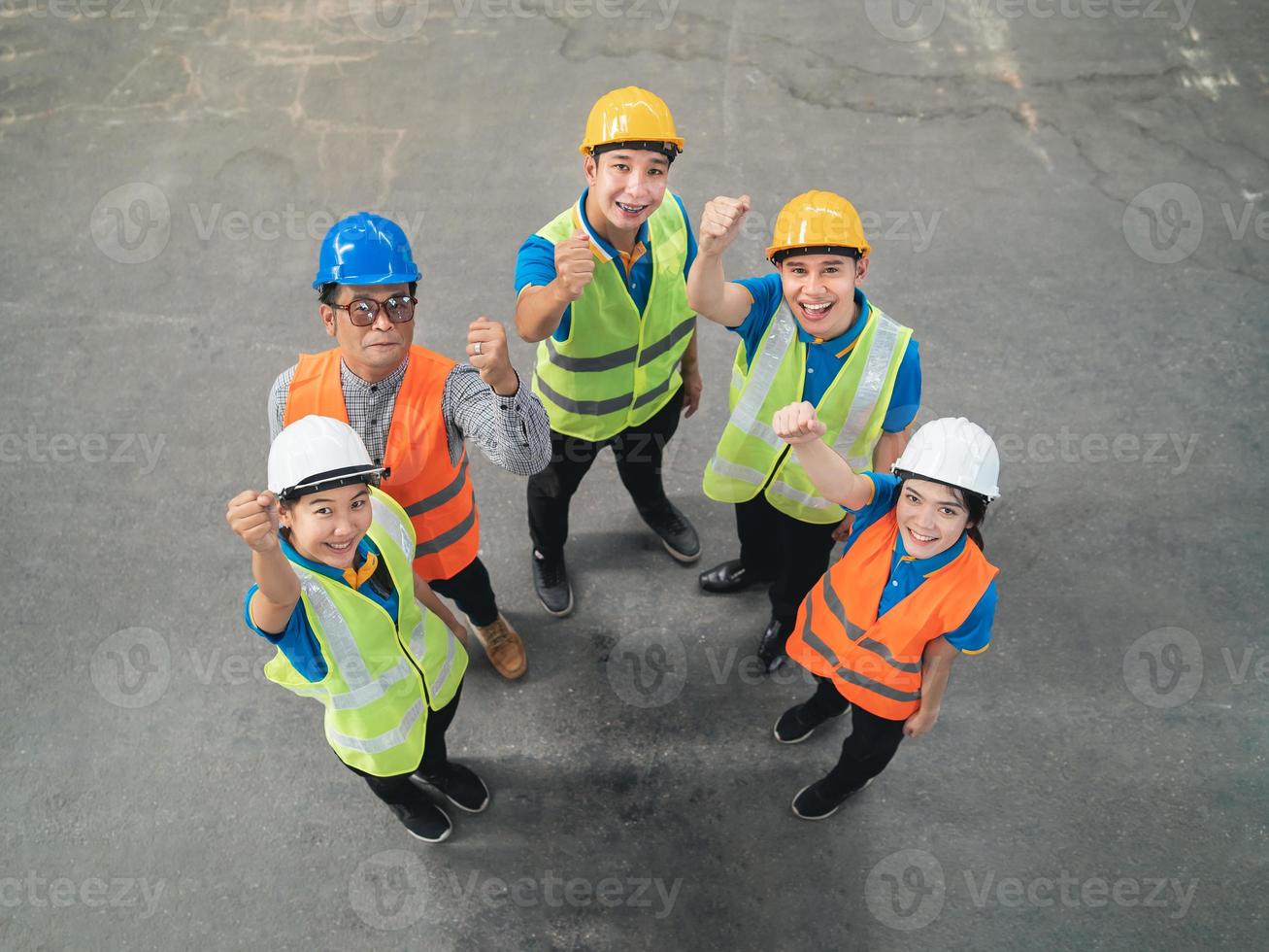 gruppe von asiatischen industrielagerarbeitern in und sicherheitssuite, die feiert oder hände hebt, stellt erfolgreiches oder deal-engagement dar. Logistik, Lieferkette und Lagergeschäft. Draufsicht der Teamwork-Einheit. foto