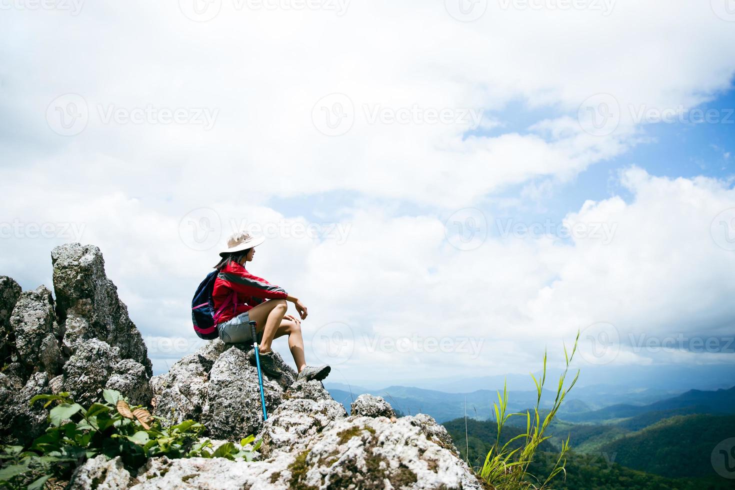 junge Wanderfrau, die auf einem Felsen sitzt, Rucksackfrau, die im Sommer das schöne Bergtal im Sonnenlicht betrachtet, Landschaft mit Sportmädchen, hohe Hügel, Wald, Himmel. Reisen und Tourismus. foto