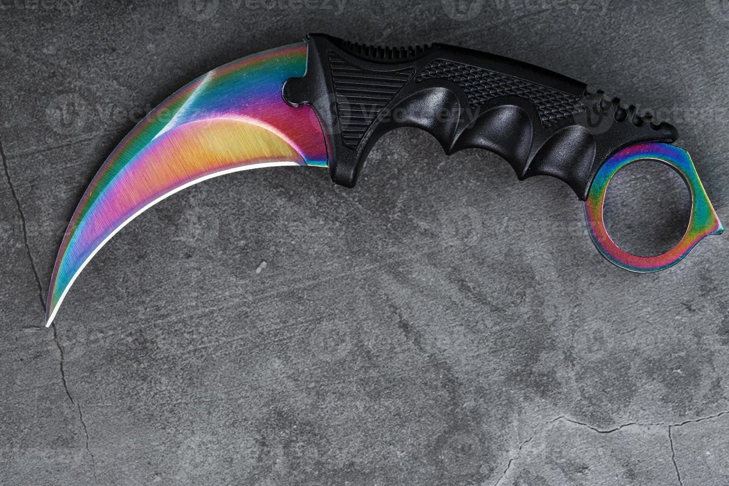 Kerambit-Dolch mit einer regenbogenfarbenen Klinge auf einem dunklen strukturierten Hintergrund. foto