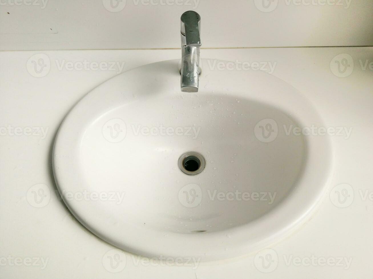 Weißes Waschbecken und silberner Wasserhahn mit Wassertropfenspuren, altes und stumpfes Bild. foto