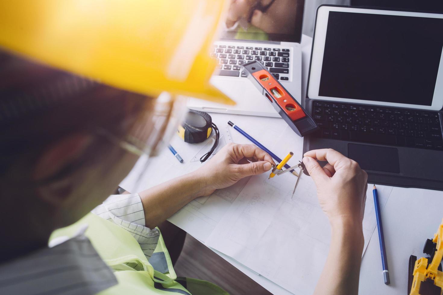 Zwei Kollegen diskutieren über Datenverarbeitung und Tablet, Laptop mit einem Architekturprojekt auf der Baustelle am Schreibtisch im Büro foto