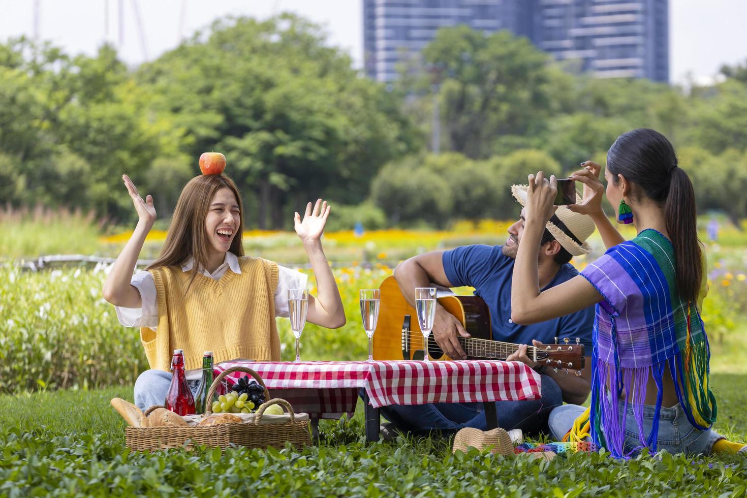 Eine Gruppe junger, vielfältiger enger Freunde, die im Garten picknicken, während sie im Sommer fröhlich und glücklich Musik im öffentlichen Park im Freien singen foto